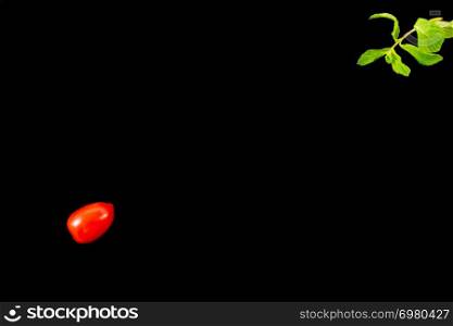 Top view of single cherry tomato on one side and mint leaves diagonally opposite isolated on a black background. Minimalist picture style with copy space for text