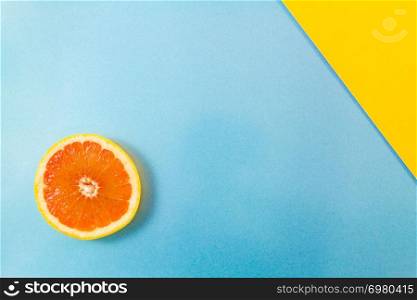 Top view of single grapefruit slice on blue and diagonal yellow background. Minimalist picture style with copy space for text