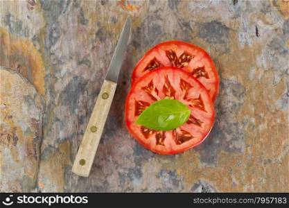 Top view of single large basil leaf on freshly sliced tomato with knife. Real stone cutting board.