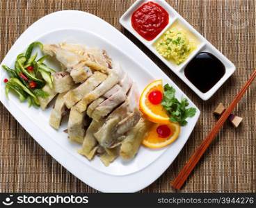 Top view of sliced roasted chicken and vegetables with dipping sauces. Bamboo mat underneath dish.