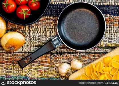 Top view of small pan, onions, garlic, pasta and fresh ripe cherry tomatoes on a rustic napkin. Ingredients and food concept