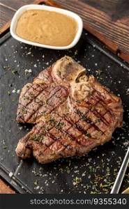 Top view of T-Bone Steak served on stone plate with sauce on the side