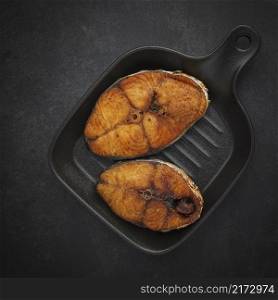 top view of tasty fried fish with black pan on dark gray, grey, black tone texture background