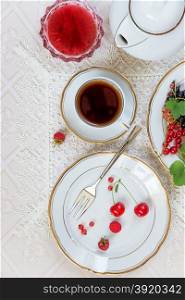 Top view of the beautifully decorated table with cup of tea, white plates with different berries, linen napkin, cutlery and jam on luxurious tablecloths