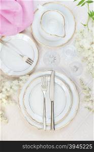 Top view of the beautifully decorated table with white plates, crystal glasses, pink linen napkin, cutlery and flowers on luxurious tablecloths