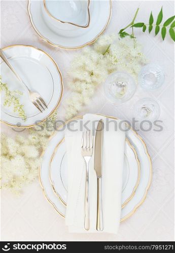 Top view of the beautifully decorated table with white plates, crystal glasses, linen napkin, cutlery and flowers on luxurious tablecloths