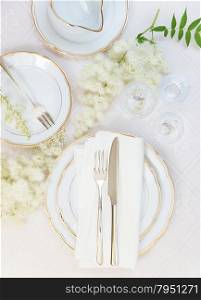 Top view of the beautifully decorated table with white plates, crystal glasses, linen napkin, cutlery and flowers on luxurious tablecloths