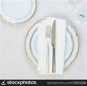 Top view of the beautifully decorated table with white plates, crystal glasses, linen napkin and cutlery on luxurious tablecloths