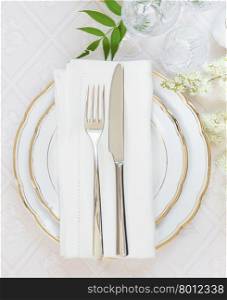 Top view of the beautifully decorated table with white plates, crystal glasses, linen napkin, cutlery and white flower on luxurious tablecloths, with space for text