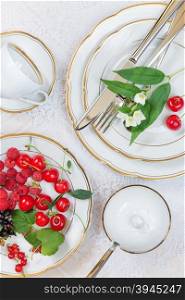 Top view of the beautifully decorated table with white porcelain plates with different berries, cutlery and flowers on luxurious tablecloths