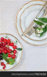 Top view of the beautifully decorated table with white porcelain plates with different berries, cutlery and flowers on luxurious tablecloths, with space for text