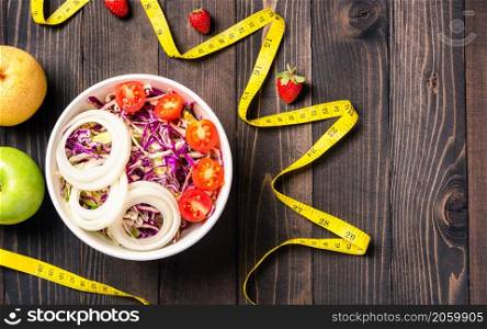 Top view of the healthy colorful salad bowl with tomatoes fresh mixed greens vegetable in a dish and measuring tape on black wooden background, Health salad snack diet food weight loss concept