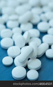 Top view of the Spilled white pills on the blue wooden surface. Focus foreground