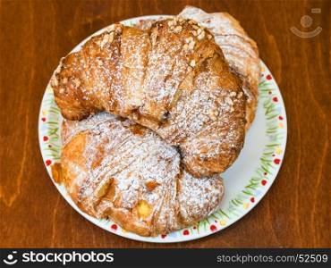 top view of three fresh italian croissants filled by vanilla and chocolate creams on wooden table