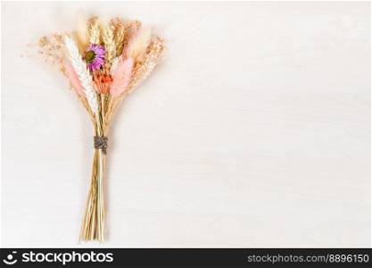 top view of tied bouquet of dried flowers and spikelets lies on light brown wooden background with copyspace