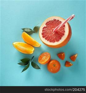 Top view of tropical exotic citrus fruits half a grapefruit, tangerines, orange slices with a plastic straw for juice on a blue paper background.. Flat lay exotic citrus fruits with green leaves and plastic straw for juice on a blue paper background.