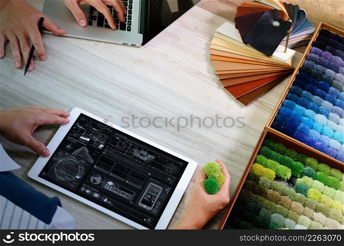 top view of two colleagues interior designers discussing data with digital tablet and new modern computer laptop with sample material on wooden desk as concept