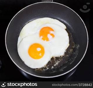top view of two fried eggs in frying pan on electric stove