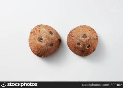 Top view of two part of natural organic brown exotic fruit coconuts on a light grey background with soft shadows and copy space. Vegetarian concept.. Two whole parts of brown natural tropical coconut fruit on a grey background.
