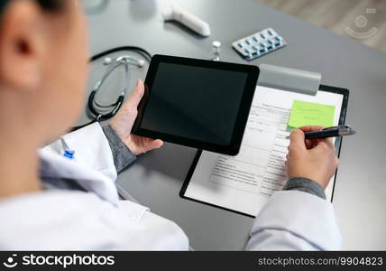 Top view of unrecognizable female doctor using tablet while working in her office