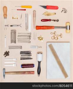 top view of various leatherwork tools and marble board on natural leather surface