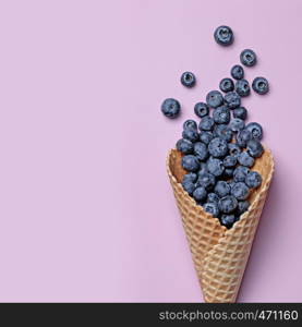 Top view of waffle cone with ripe blueberries on pastel pink background, flat lay