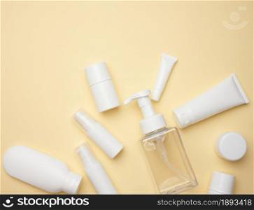top view of white cream tubes, cosmetic dispenser, empty jars and with hand cream, transparent dispenser on a light yellow background. Branding of cosmetic products, mock up