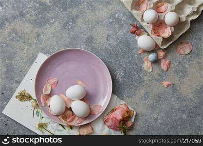 top view of white eggs with dried flowers on stone background. White eggs on pink plate