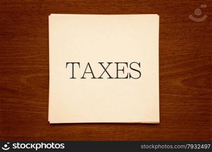 "Top view of white paper cards with word " TAXES " putting on natural wood background, vignette and sepia tone image"