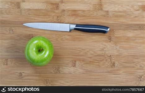 Top view of whole green apple and cutting knife on natural bamboo board