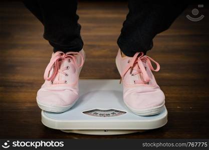 Top view of woman feet wearing pink sneakers on bathroom weight scale. Fit, dieting, fat loss concept.. Woman with pink sneakers on bathroom weight scale