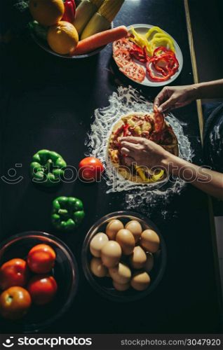 Top view of woman hand put topping on homemade pizza.