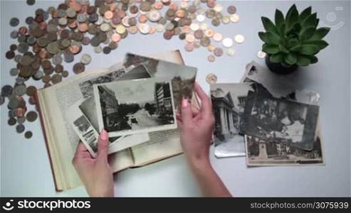 Top view of woman looking through old photos, postcards and vintage coins, book on the white table