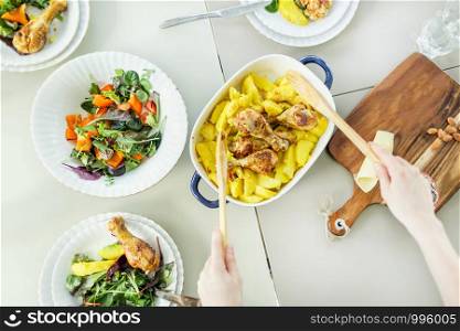 Top view of woman preparing roasted chicken with potato side dish, plates of vegetable salad on table. Top view of woman preparing roasted chicken with potato side dish