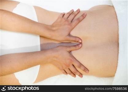 Top view of woman receiving a back massage in a spa center. Female patient is receiving treatment by professional therapist.. Young woman receiving a back massage in a spa center