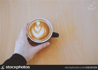 Top view of woman?s hand holding cup of hot cappuccino coffee on the wooden table with copy space