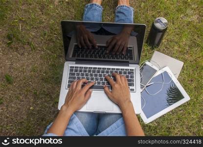 Top view of women sitting in the park on the lawn with a laptop, notebook and smartphone and hands on the keyboard