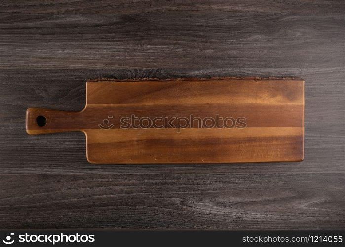 Top view of wooden cutting board on old dark wood countertop.
