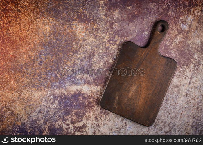 Top view of wooden cutting board on old rusty metal countertop.