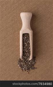 Top view of wooden scoop with chia seeds against brown vinyl background.