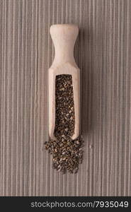 Top view of wooden scoop with chia seeds against brown vinyl background.