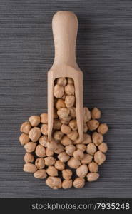 Top view of wooden scoop with chickpeas against grey vinyl background.