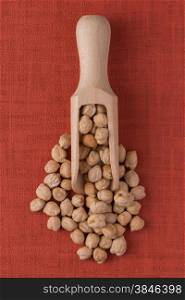 Top view of wooden scoop with chickpeas against red vinyl background.