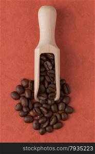 Top view of wooden scoop with coffee beans against red vinyl background.