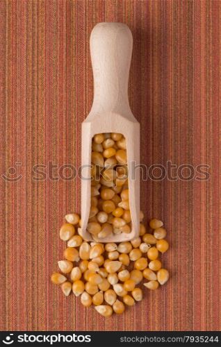 Top view of wooden scoop with corn against red vinyl background.