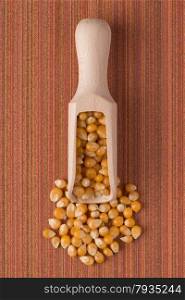 Top view of wooden scoop with corn against red vinyl background.