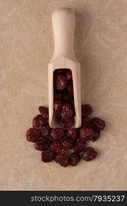 Top view of wooden scoop with dried cranberries against beige vinyl background.