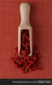 Top view of wooden scoop with dry red goji berries against red vinyl background.