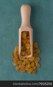 Top view of wooden scoop with golden raisins against blue vinyl background.