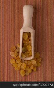 Top view of wooden scoop with golden raisins against red vinyl background.